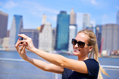Buy stock photo Woman, smartphone and smile for selfie in city, sightseeing tourist and happy female person in New York. Memories, social media post on technology with influencer, blue sky and buildings in summer