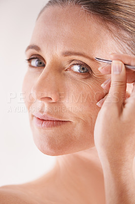 Buy stock photo Beauty, tweezers and portrait of a mature model on white background for facial grooming or hair removal. Spa, salon and face of female person in studio plucking or tweezing eyebrows for skincare glow