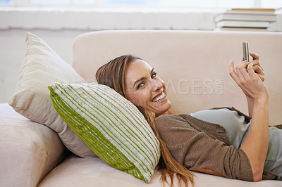 Buy stock photo Portrait of an attractive woman using a mobile phone while relaxing on the sofa at home