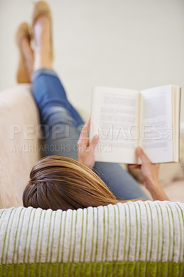 Buy stock photo Shot of a woman reading a book while lying on the sofa at home