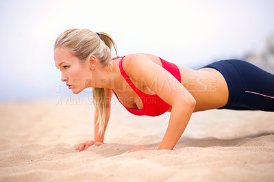Buy stock photo Shot of a young woman in sportswear doing pushups on the beach