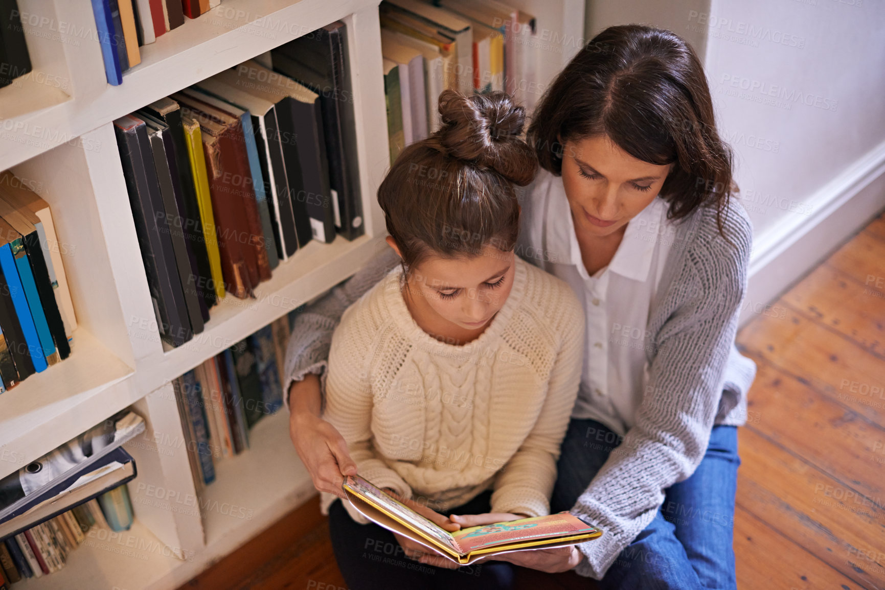 Buy stock photo Mother, daughter and reading with book for literature, story or knowledge by bookshelf at home. Top view of mom helping child or girl with novel for education or learning on the floor in library