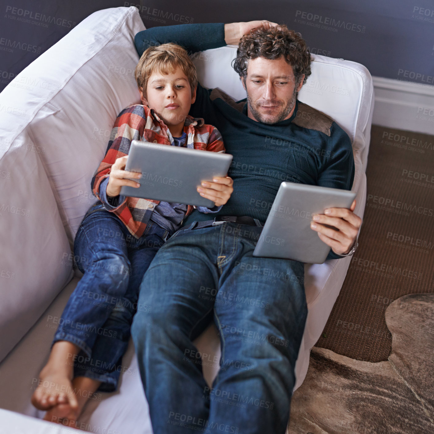 Buy stock photo Shot of a father son lying on the couch together while using digital tablets