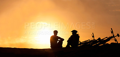 Buy stock photo Silhouette of a couple watching the sunset with their bicycles beside them at the beach