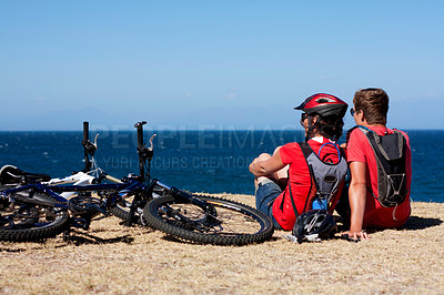 Buy stock photo A young couple sitting at the beach alongside their bicycles