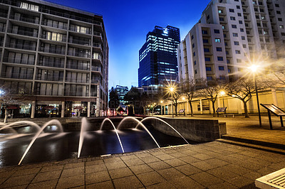 Buy stock photo Night, cityscape and urban buildings at dark with lights in Cape Town outdoor with no people. Street, lighting and city infrastructure with fountain and skyline at evening outdoors with a road