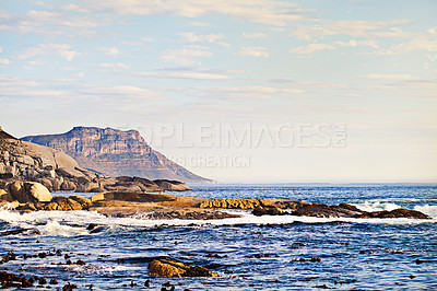 Buy stock photo Mountains, ocean and nature with waves at beach for environment, landscape and blue sky. Calm, summer and seascape with sunrise on horizon at coastline for tropical, clouds and water on rock surface