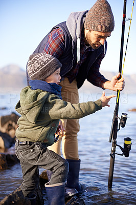 Buy stock photo Father, fishing and teaching for young boy, rocks and bonding for activity by ocean. Sea, rod and learning how to fish for childhood development, winter and hobby together while on seaside vacation