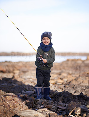 Buy stock photo Portrait, fishing rod and happy boy on shoreline, rocks and smile for activity by ocean. Sea, catch and learning how to fish for childhood development, young child and hobby while on seaside vacation