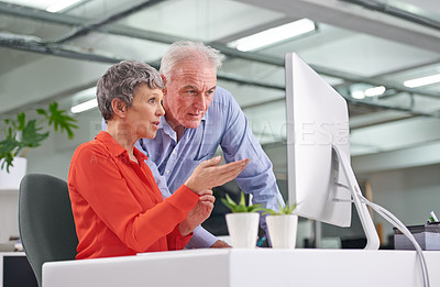 Buy stock photo Shot of two mature business colleagues discussing work at a desktop computer
