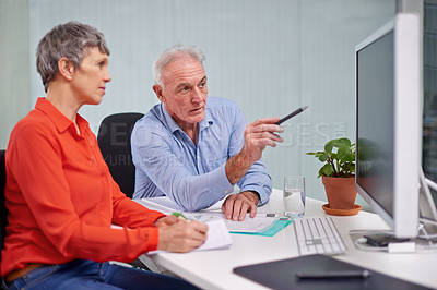 Buy stock photo Shot of two mature business colleagues discussing work at a desktop computer