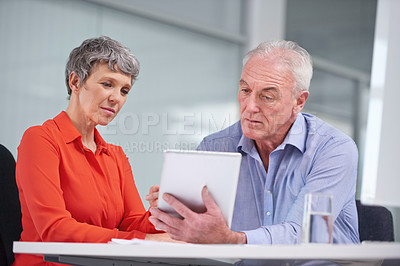 Buy stock photo Shot of two mature business colleagues sitting with a digital tablet and discussing work