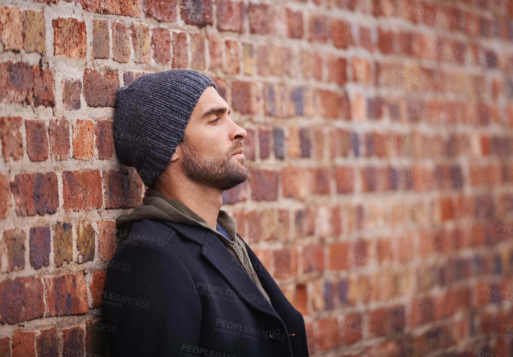 Buy stock photo Cropped shot of a fashionable man leaning against a brick wall in an urban setting
