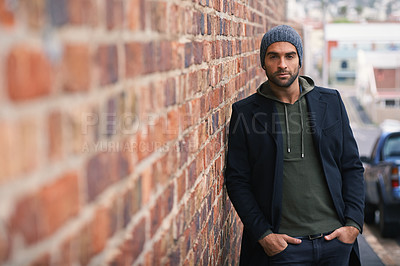 Buy stock photo Portrait, confidence and man on brick wall in city in casual clothes, outfit or fashion for winter outdoor. Serious, cool and stylish person in urban town in beanie, hoodie and trendy jacket in Spain