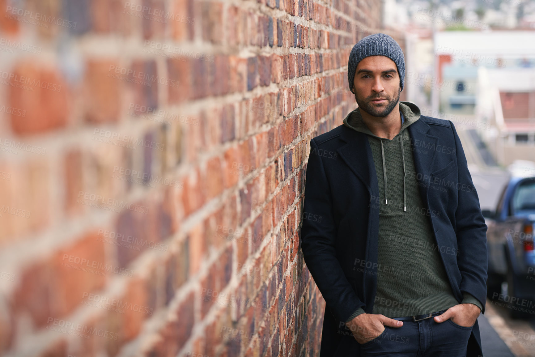 Buy stock photo Portrait, confidence and man on brick wall in city in casual clothes, outfit or fashion for winter outdoor. Serious, cool and stylish person in urban town in beanie, hoodie and trendy jacket in Spain