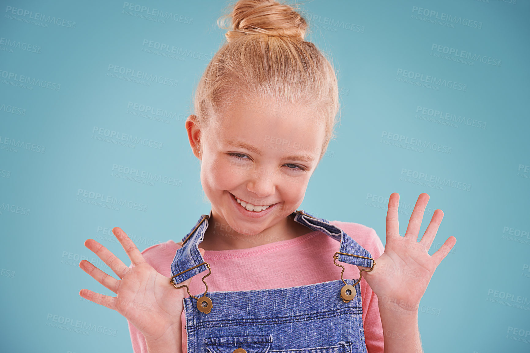 Buy stock photo Child, portrait and happy in studio with confidence in dungarees on blue background, good mood or mockup space. Girl, school student and smile for playful hands or expression, childhood or positivity