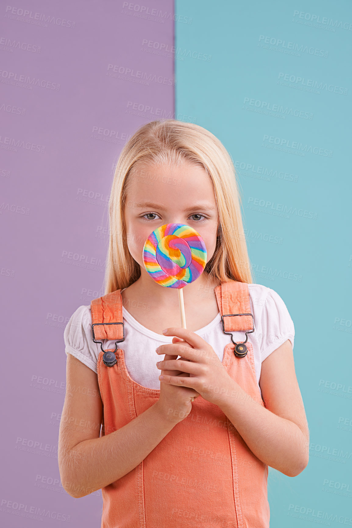 Buy stock photo Studio, girl and hiding with lollipop, dessert and playful for snack and childhood. Child, sweets and yummy candy for tasty, eating and happiness on vibrant split pastel pink and blue background