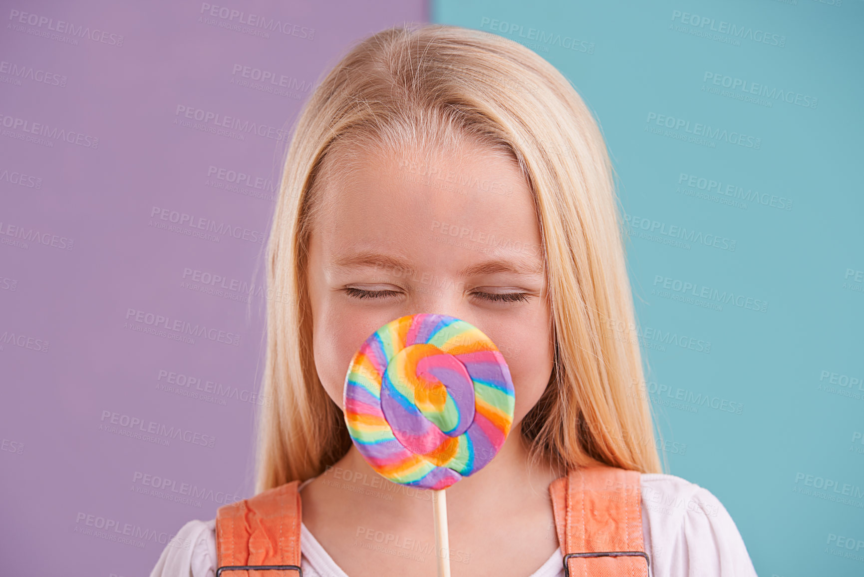 Buy stock photo Child, lollipop and candy dessert in studio fr party snack at carnival or rainbow swirl, eating or sweets. Female person, happy and hiding as split purple or blue background for hungry, treats or fun