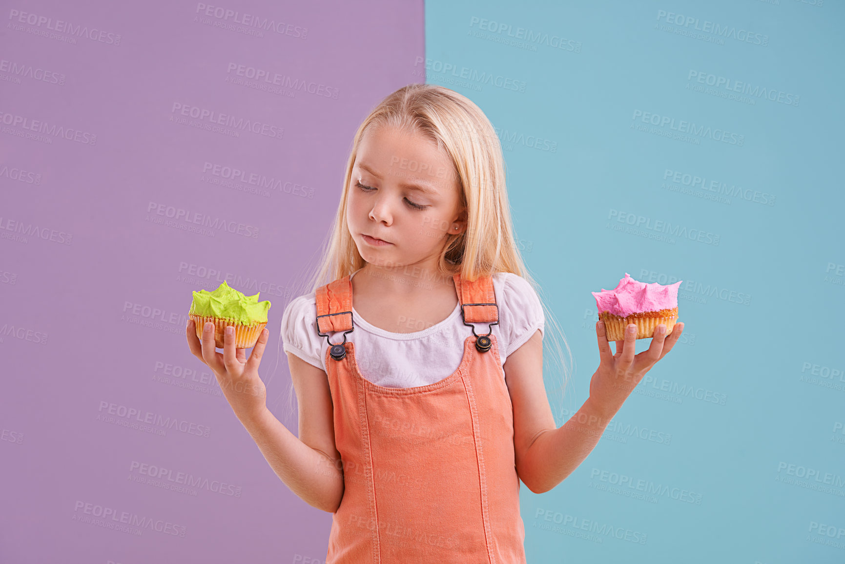 Buy stock photo Studio, girl and choice with cupcakes, dessert and decision for snack and childhood. Child, sweets and yummy selection for tasty, eating and choosing on vibrant split pastel pink and blue background