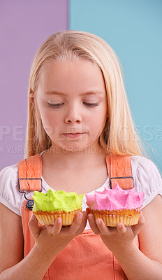 Buy stock photo Studio, girl and decision with cupcakes, desert and choice for snack and childhood. Child, sweets and yummy selection for tasty, eating and choosing on vibrant split pastel pink and blue background