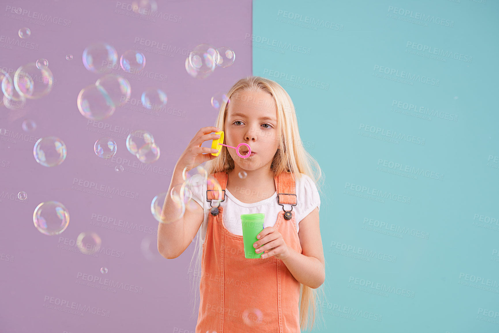 Buy stock photo Child, blowing bubbles and playing in studio as holiday activity for leisure, childhood development or mockup space. Female person, kid and toy or split purple with blue background, innocent or fun