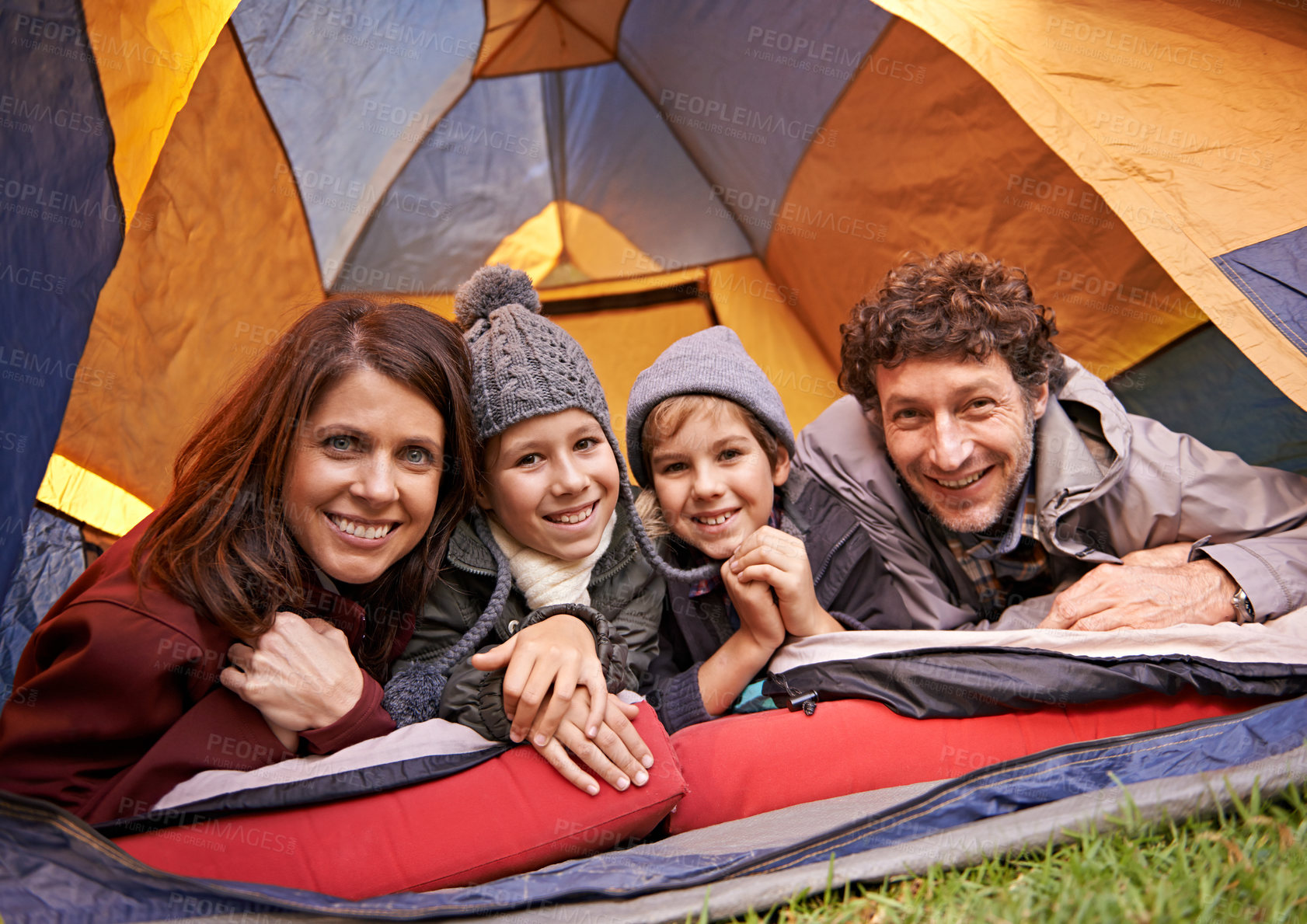 Buy stock photo Portrait of smiling family of four relaxing in tent on a camping holiday