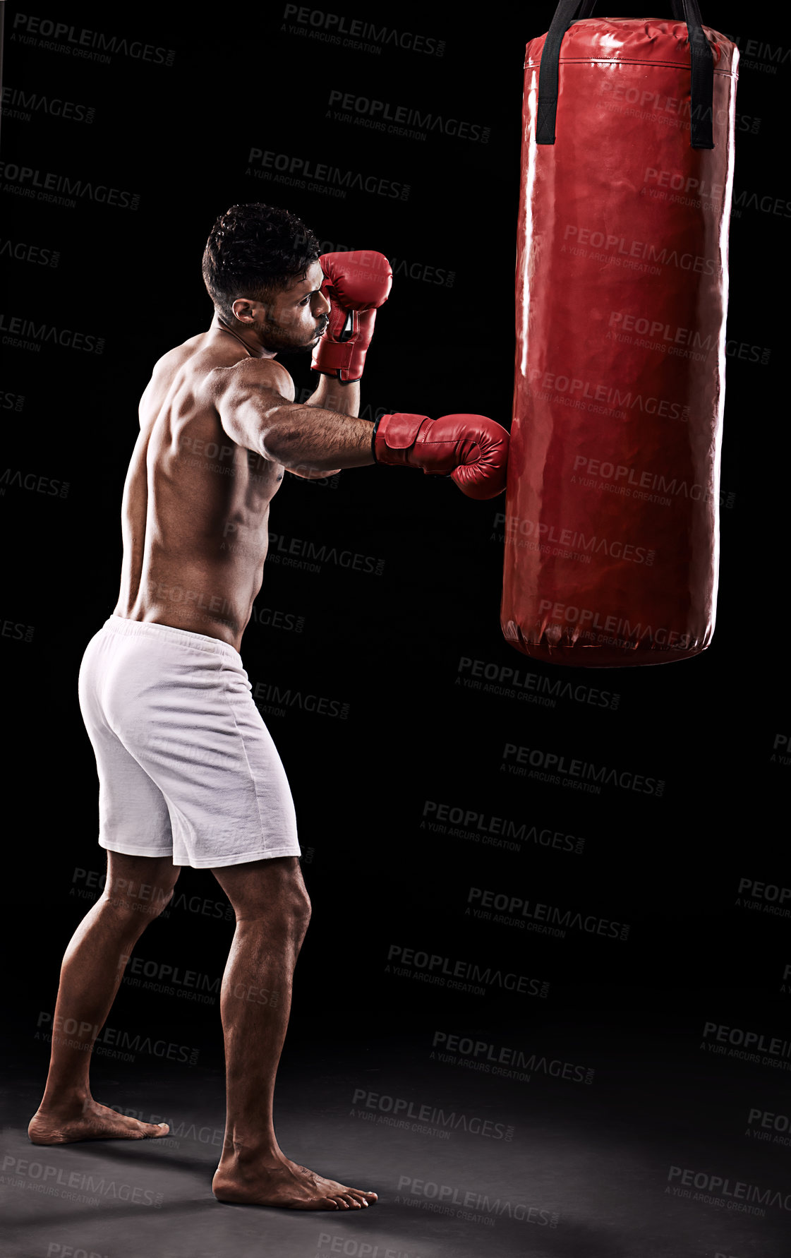 Buy stock photo Studio shot of handsome young man and his punching bag against a black background