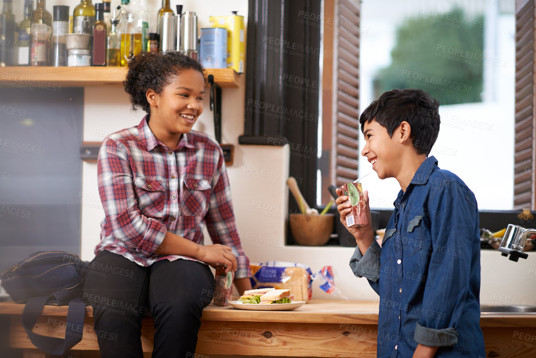 Buy stock photo Shot of two young teenagers enjoying a snack together in the kitchen