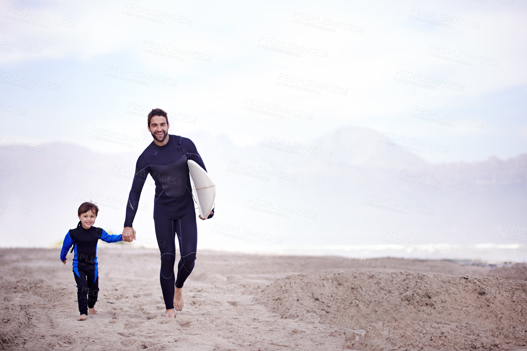 Buy stock photo A father walking along the beach with his young son before a surfing lesson
