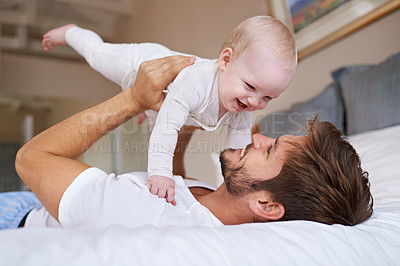 Buy stock photo Shot of a father lying on a bed holding his baby girl up in the air