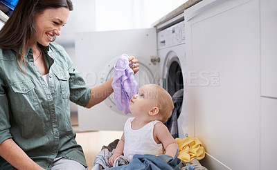 Buy stock photo Shot of a mother and her baby girl playing while doing laundry