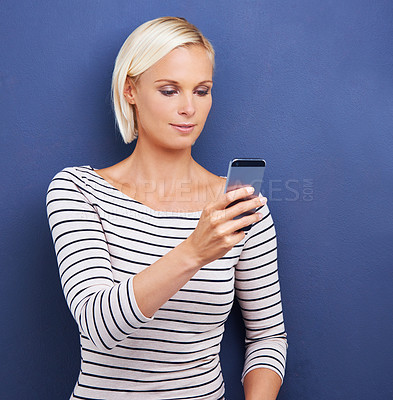 Buy stock photo Blonde woman, typing and browsing with phone for social media, communication or networking on a blue studio background. Young female person on mobile smartphone for online chatting or texting on app