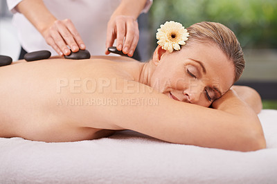 Buy stock photo Woman, hands and hot stone massage with masseuse at spa, flower for natural treatment and wellness with zen. Calm, peace and luxury bodycare with warm rocks for detox, self care and holistic healing