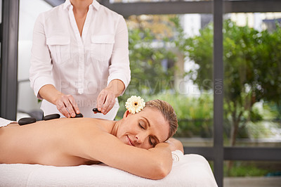 Buy stock photo Woman, hands and hot stone massage at spa with masseuse, flower for natural treatment and wellness with zen. Calm, peace and luxury bodycare with warm rocks for detox, self care and holistic healing