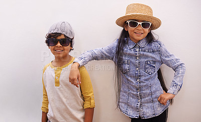 Buy stock photo Children, portrait and fashion or sunglasses for style and looking cool on a wall or white background at home. Happy sibling, girl and boy with trendy clothes, casual and shades for fun or confidence