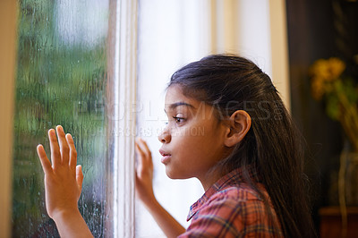 Buy stock photo Shot of a cute little girl looking out the window on a rainy day