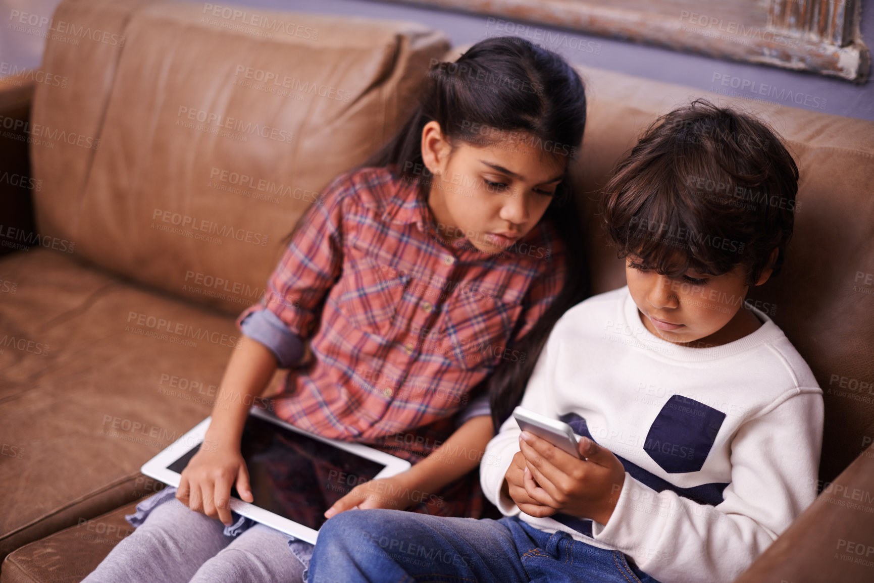 Buy stock photo Shot of two siblings playing with their digital devices at home