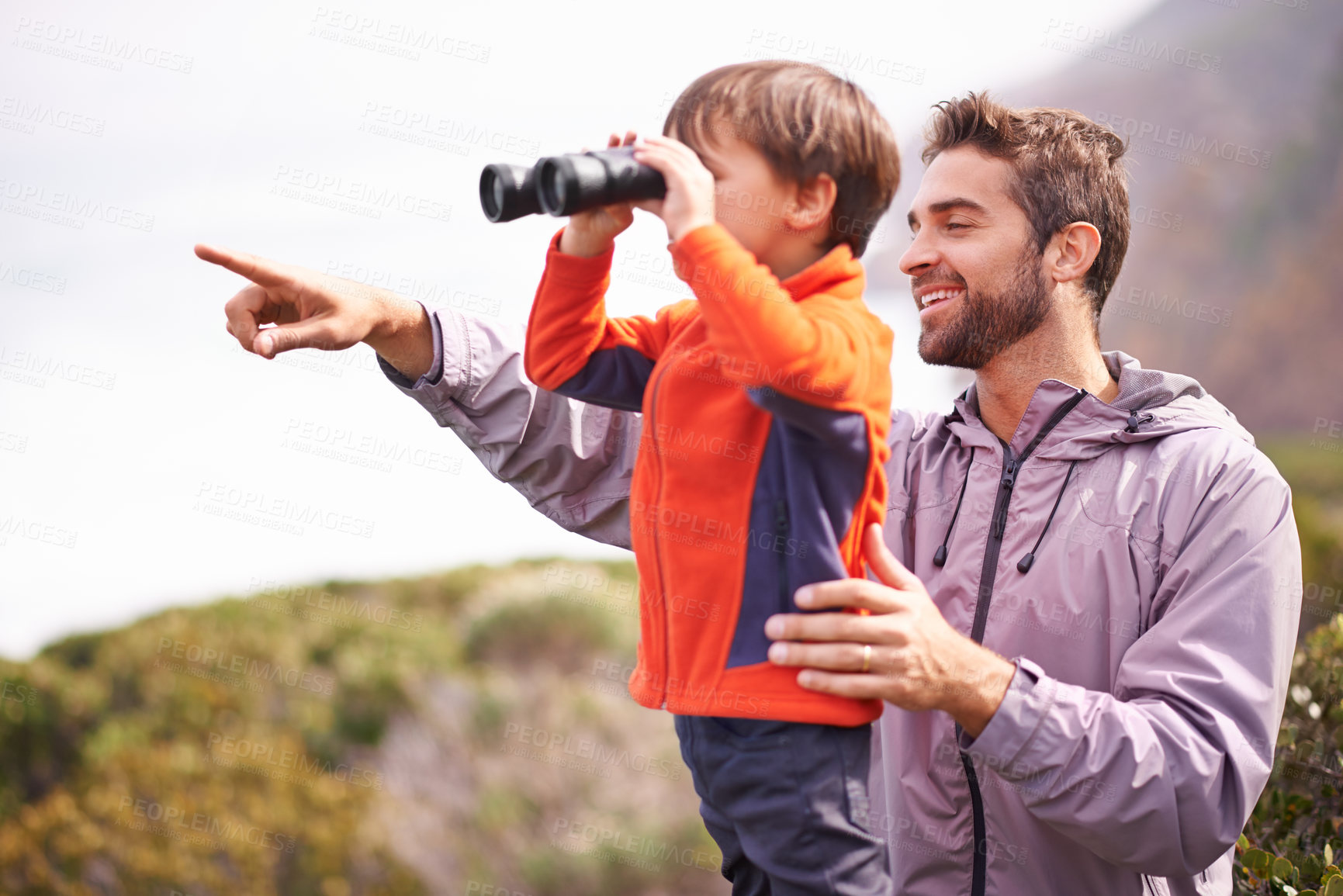 Buy stock photo Shot of a father pointing to something while his son looks through binoculars on a hike together