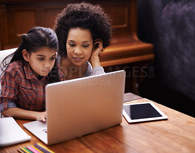 Buy stock photo Shot of a little girl using a laptop to do her homework while her mother sits by