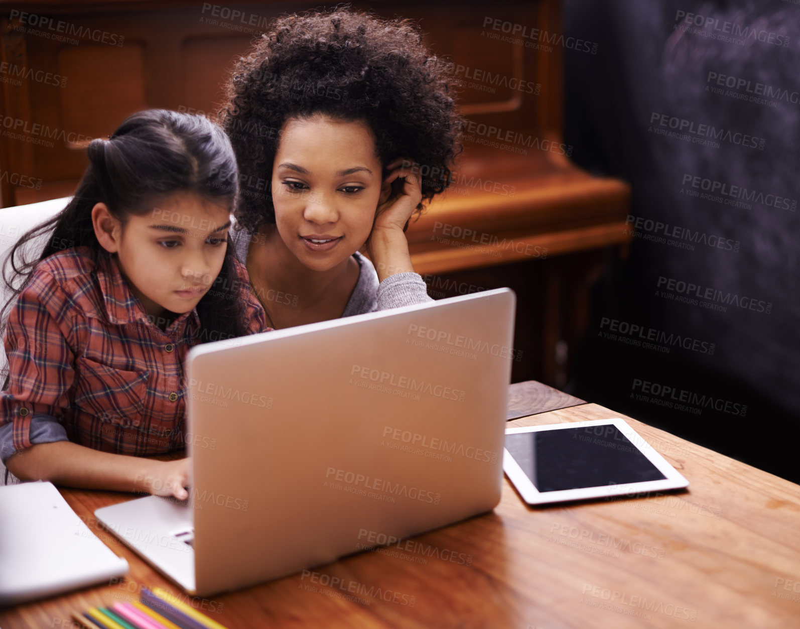 Buy stock photo Shot of a little girl using a laptop to do her homework while her mother sits by