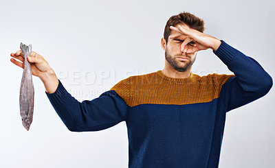 Buy stock photo Studio shot of a man showing disgust while holding a smelly fish