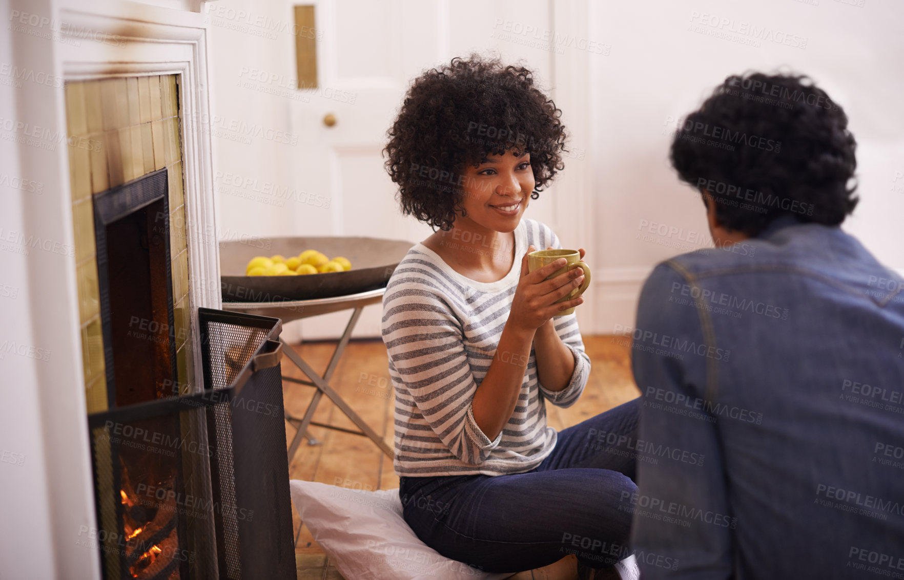 Buy stock photo Coffee, conversation and young couple in living room by fireplace bonding together in winter. Happy, love and man and woman drinking cappuccino, latte or espresso in lounge at modern apartment. 