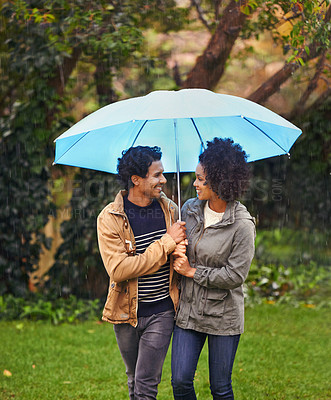 Buy stock photo Cropped shot of an affectionate young couple walking under an umbrella