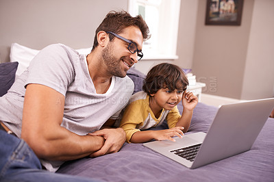 Buy stock photo Shot of a father and son using a laptop while lying on bed