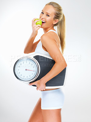 Buy stock photo Shot of a young woman holding a scale and eating an apple