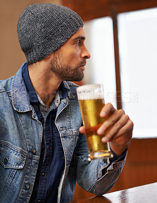 Buy stock photo Shot of a handsome young man  drinking a beer at the bar