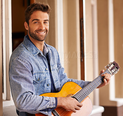 Buy stock photo Portrait of a handsome young man relaxing on the patio while playing a guitar