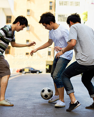 Buy stock photo Friends in street playing football together for sports, fun and happy energy with urban games in Korea. Games for kids, friendship and teen group in road with soccer ball, weekend time in Asian city.