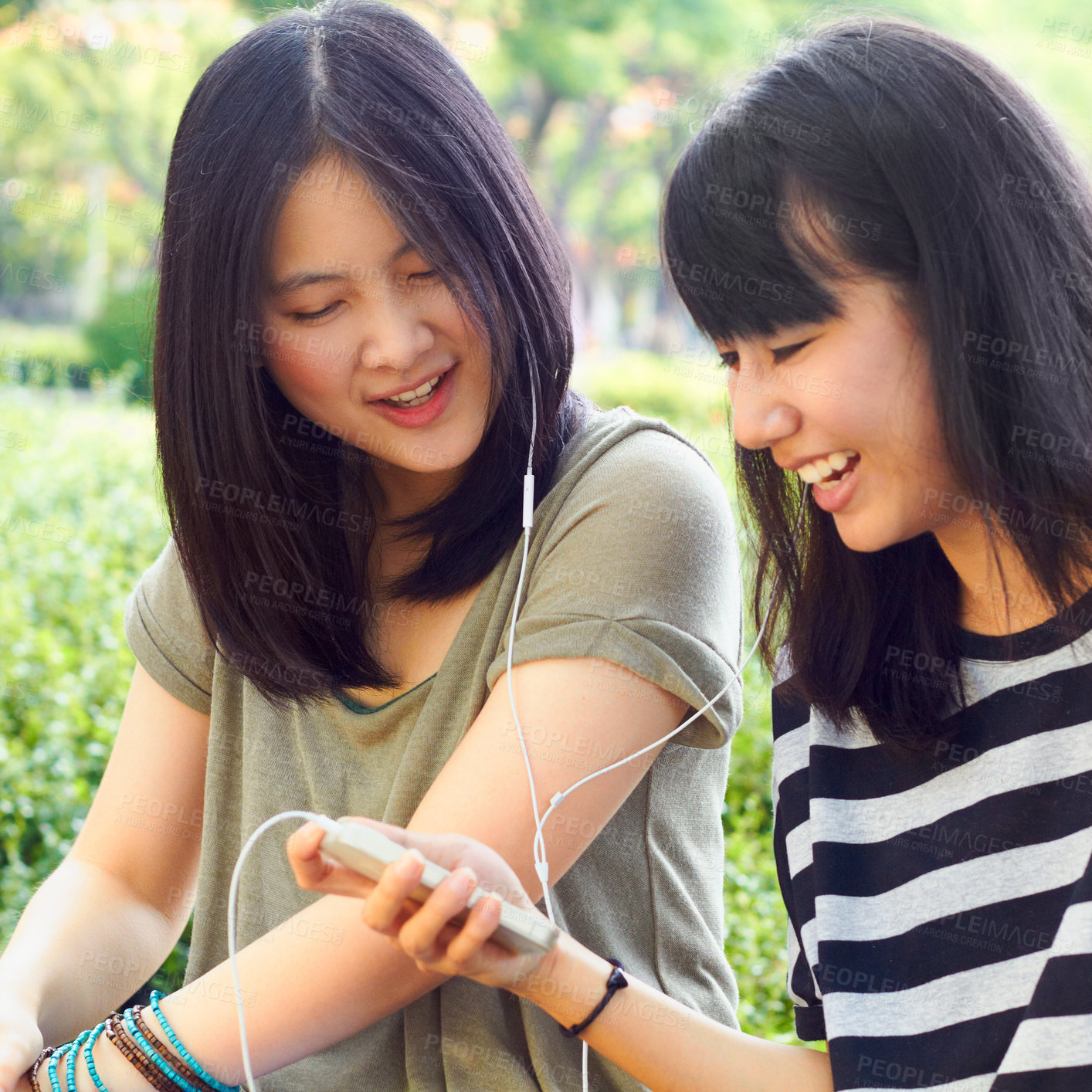 Buy stock photo Asian women, students together and earphones with comic laugh, funny music video and meme at campus. Japanese girl, friends and audio streaming with smartphone, sharing and listen with smile in park