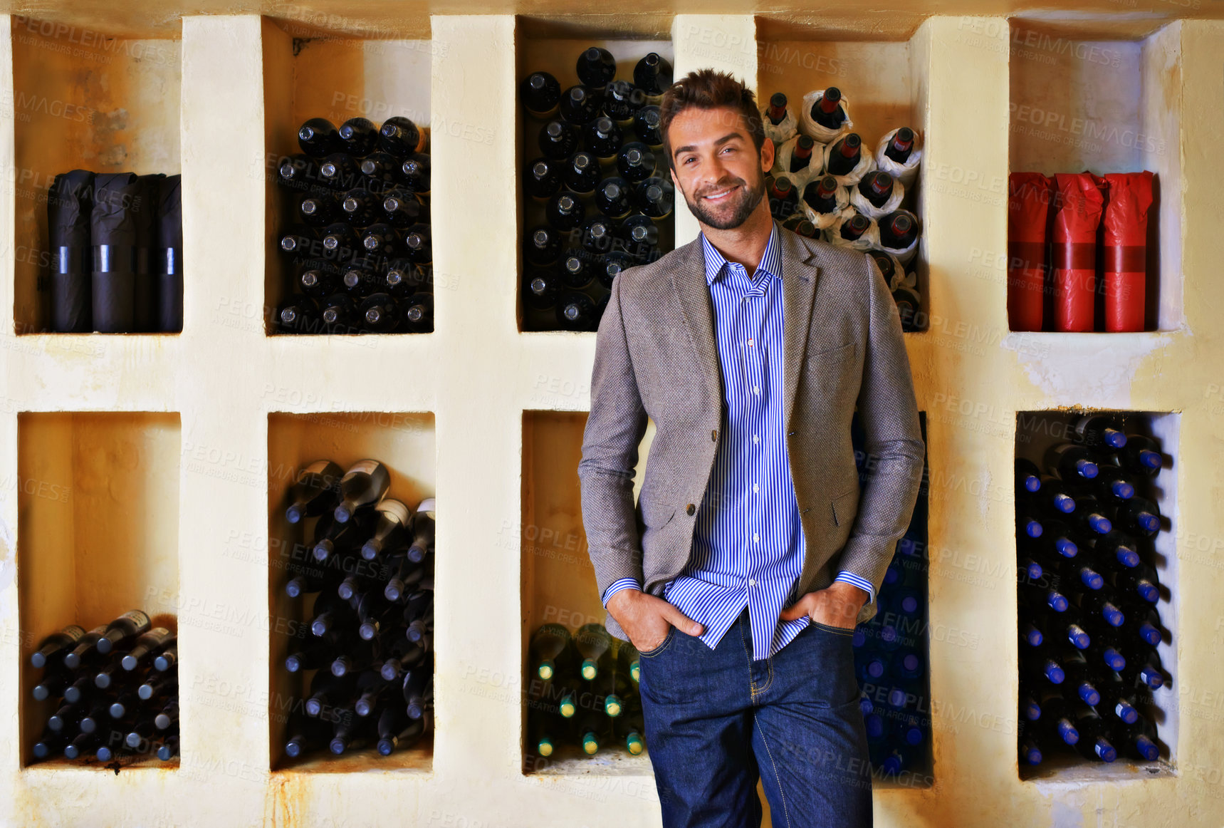 Buy stock photo A young man standing in front of a rack full of wine